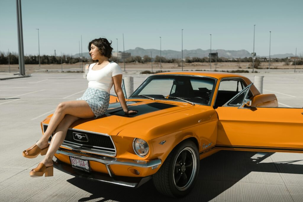 Woman in a retro outfit sits on a vintage orange Ford Mustang in Los Angeles.